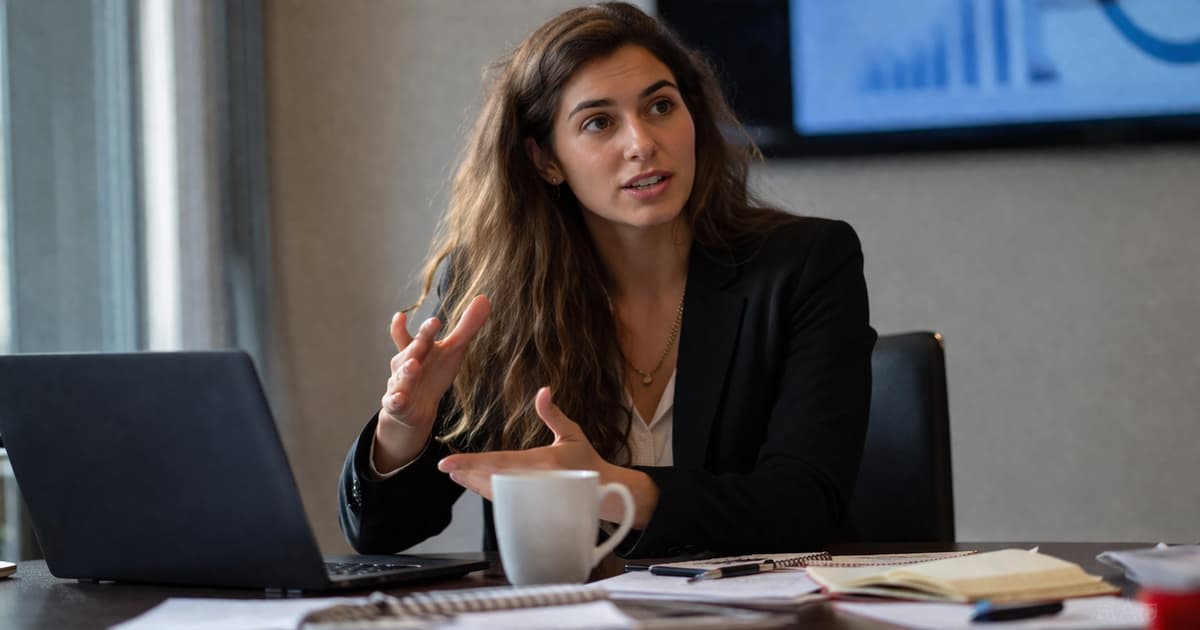 خبيرة تسويق عربية تشرح تجربة مهنية حقيقية أثناء اجتماع عمل أمام لابتوب، تمثل قوة المحتوى الشخصي مقابل الرسائل المؤسسية العامة على لينكدإن